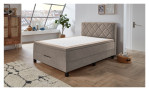 Boxspringbett Josh aus einem Mikrofaser Bezug in Beige mit schwarzen Füßen. Auf einem dekorierten Hintergrund.